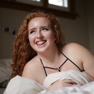 Red Hot Suz posing lying on one shoulder with bare shoulders and a mane of red hair