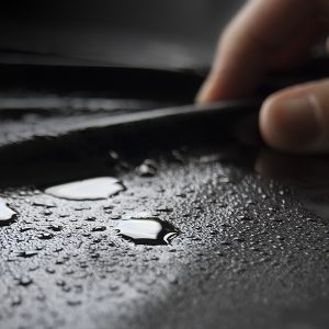 Fingers stoking the source of a black fluid proof sheet covered in moisture