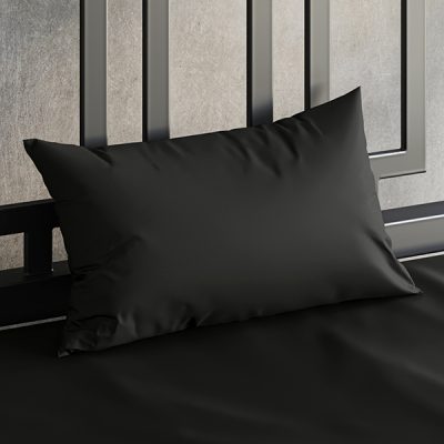 Close up of a Sheets of San Francisco Black waterproof pillow case on a bed covered in a Black Sheets of San Francisco fluid proof fitted sheet and against a black metal bedhead with the polished concrete wall behind showing through.